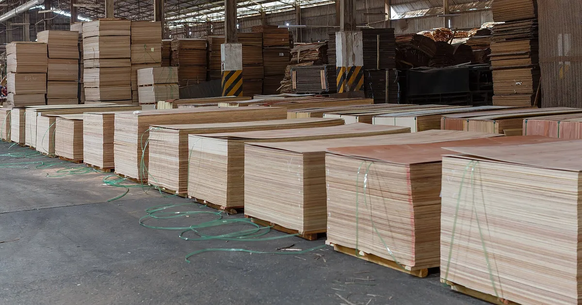 Bundles of finished plywood panels stacked on pallets in a mill warehouse, with the panel edges facing the aisle