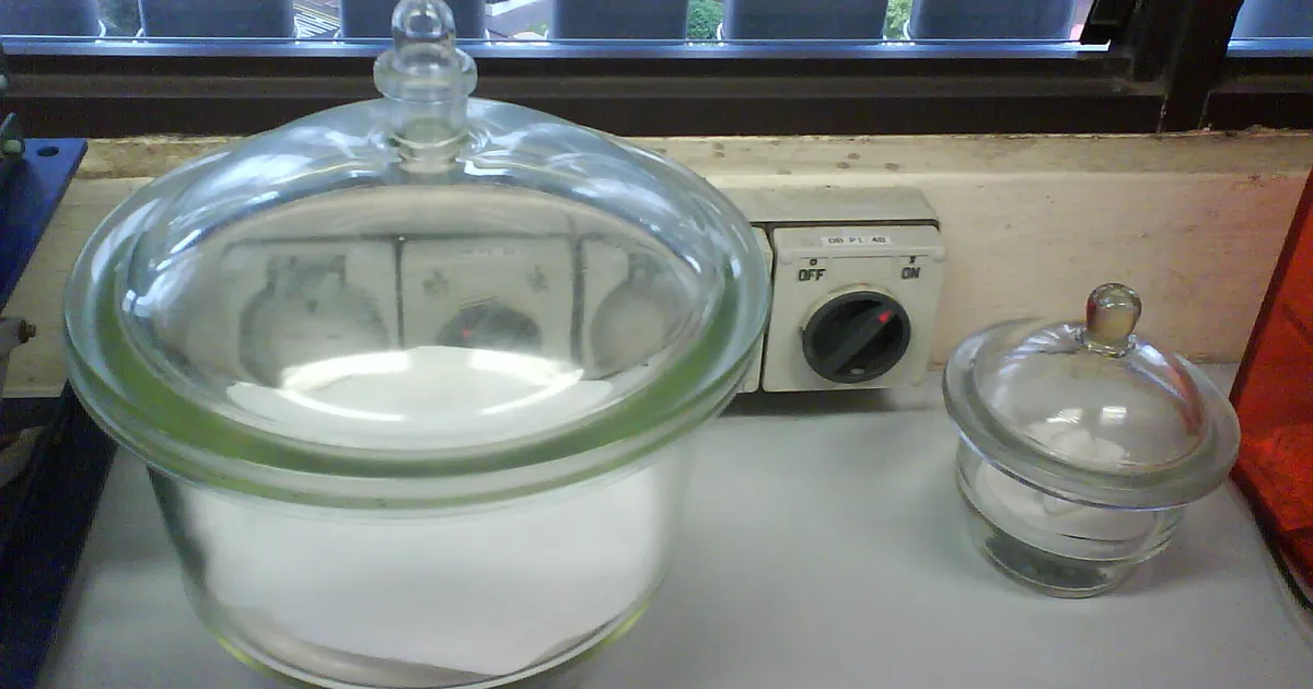 Two glass laboratory desiccators on a bench, one large with a lid and one small