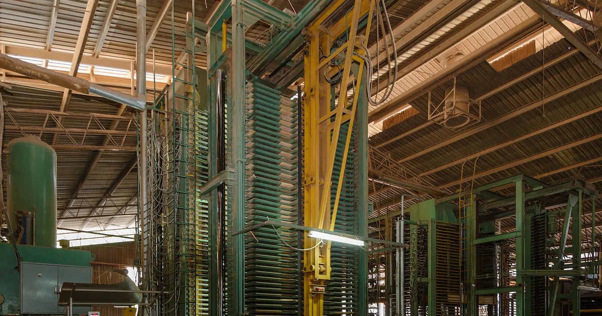 Tall multi-opening hydraulic hot press with stacked platens inside a plywood mill